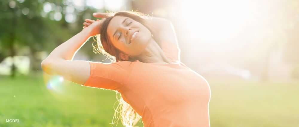 woman in orange shirt stretching in the sunlight against a green field