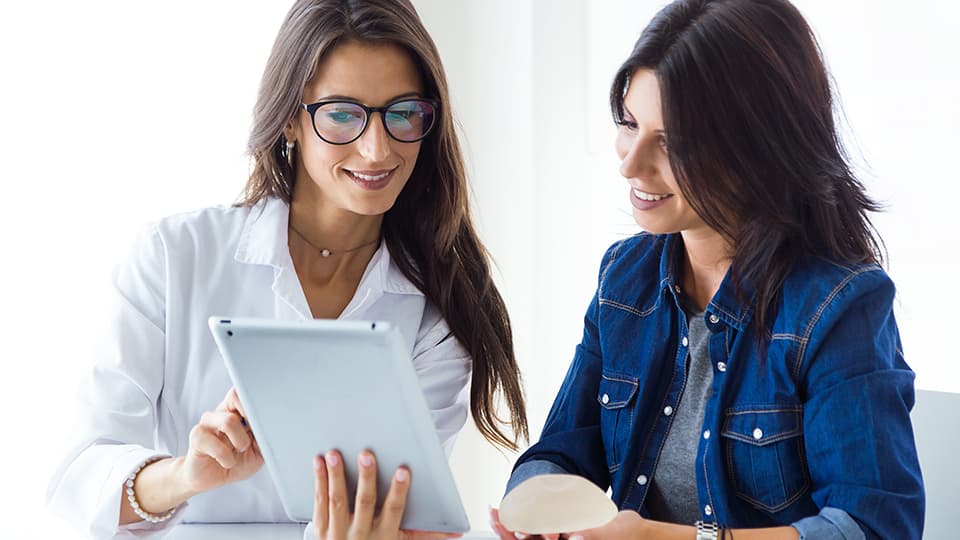 woman holding breast implant consulting with nurse looking at ipad together