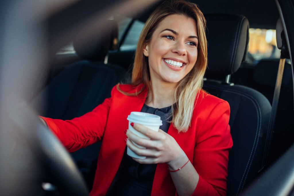 Photo of a smiling business woman in the car drinking coffee.