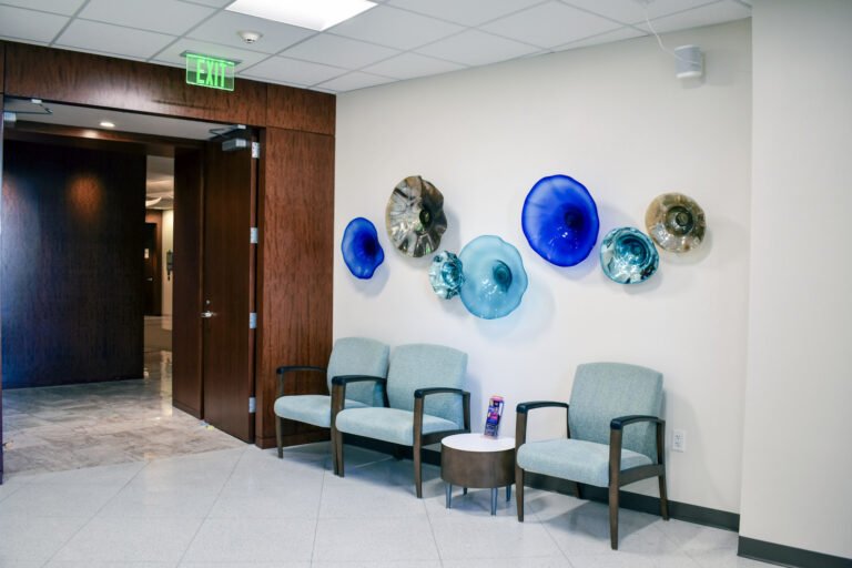 Waiting room with glass art on the walls in shades of blue and three upholstered blue chairs.