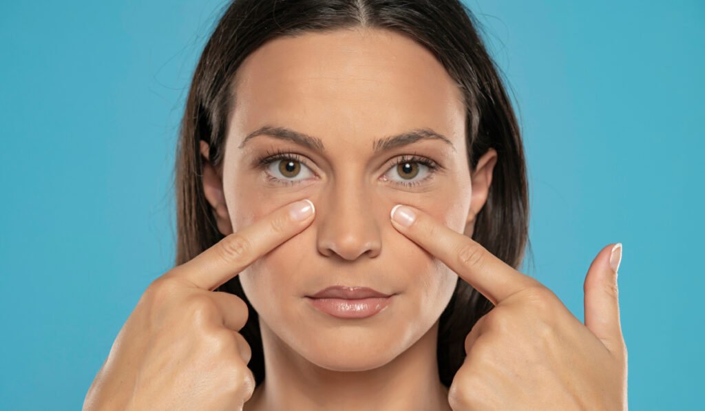 Woman touching skin under eyes on blue background