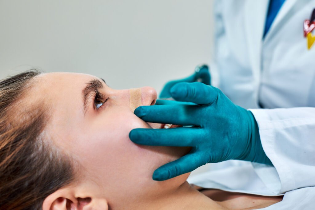 Woman getting her bandages removed by her rhinoplasty surgeon