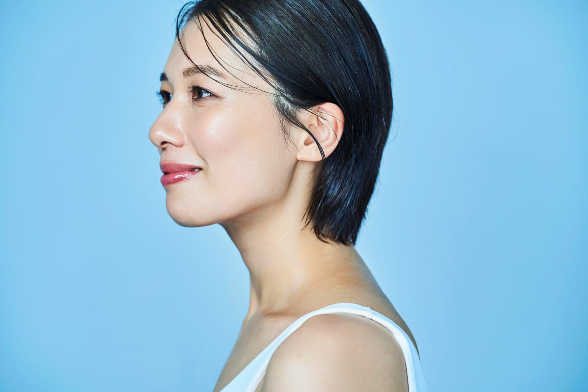 Short-haired asian woman looking off to the side in a studio portrait with a blue background