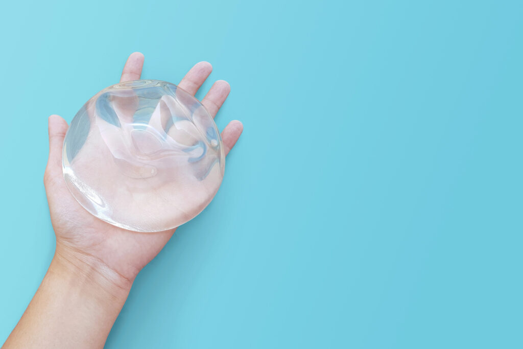 Hand holding a breast implant against a blue studio background